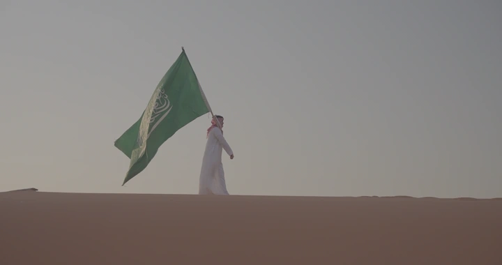 شخص يحمل علم السعودية في صحراء النفود، لقطة جانبية.