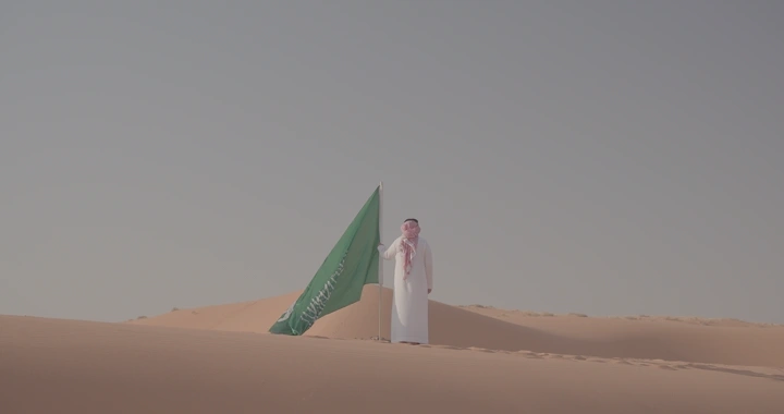 رجل يقف بجانب علم السعودية في النفود، لقطة بعيدة.