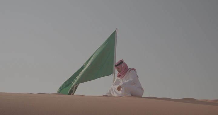 رجل يجلس في الصحراء مع علم السعودية، لقطة نهارية.
