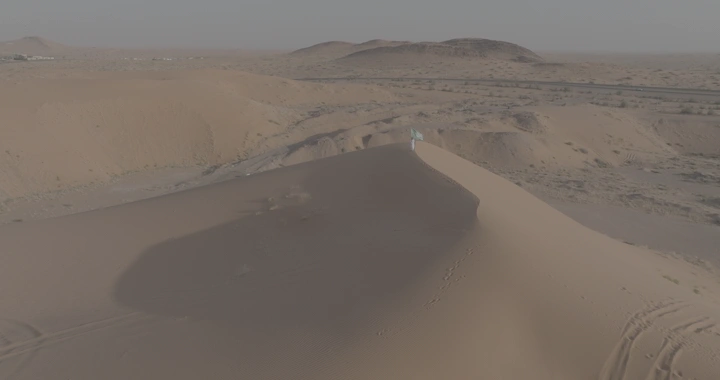 رجل يقف فوق كثبان رملية يحمل العلم السعودي، لقطة جوية.