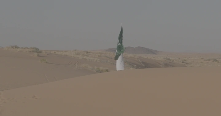 رجل يحمل علم السعودية في النفود، لقطة بعيدة.