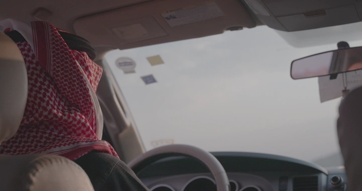 شخص يرتدي شماغ يقود سيارة ويستخدم الهوكي توكي، لقطة داخلية.