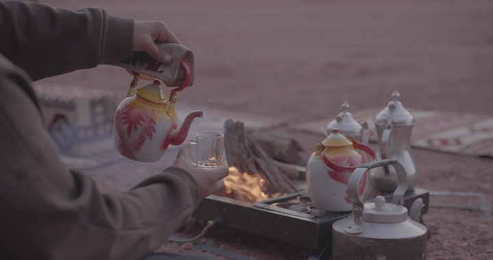 رجل يصب الشاي الأحمر في الصحراء، لقطة مقربة.