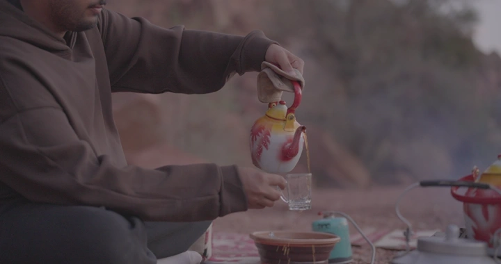 رجل يصب الشاي في كوب زجاجي في الهواء الطلق، لقطة مقربة.