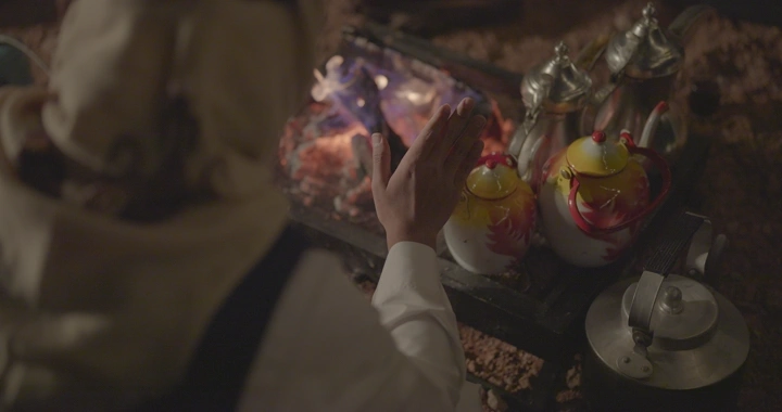 رجل يدفي يديه على الحطب بجانب دلال القهوة، لقطة قريبة.