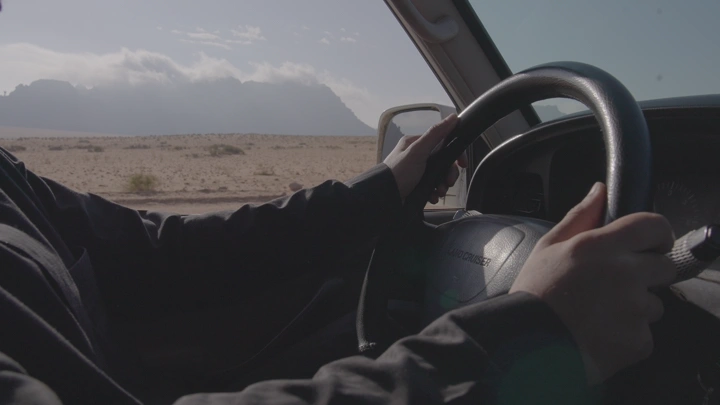 رجل يقود سيارة في الصحراء نهارًا، لقطة من الداخل.