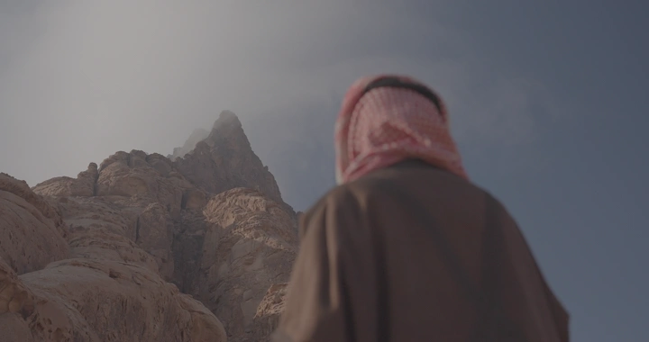 رجل ينظر إلى قمة جبل محاطة بالغيوم، لقطة من الخلف.