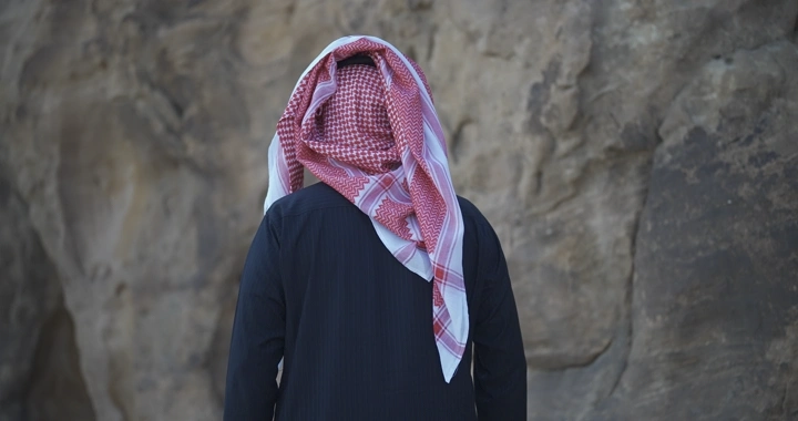 رجل يرتدي شماغ يقف أمام جبل، لقطة خلفية.