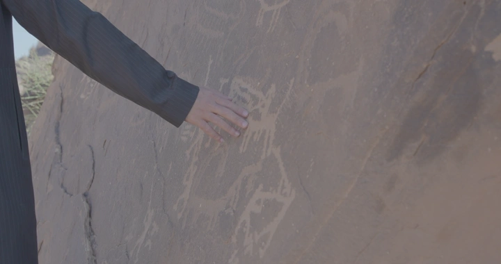 يد تلمس نقوش ثمودية على جبل في حائل، لقطة قريبة.