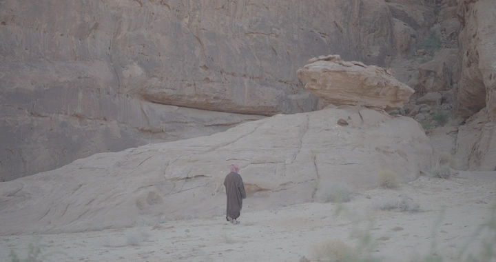 رجل يرتدي بشت شتوي يمشي في الصحراء، لقطة طبيعية.