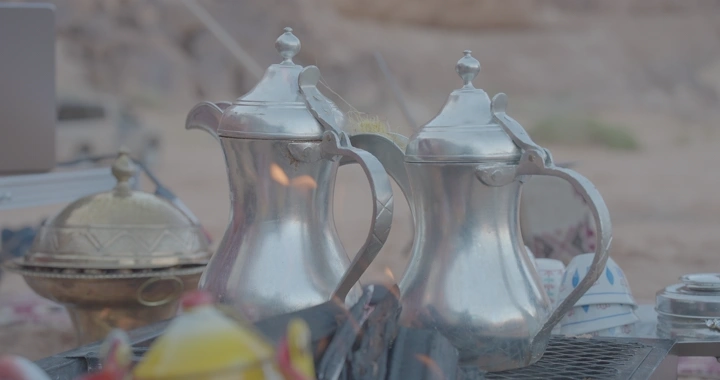 دلة قهوة فضية على الحطب في الصحراء، لقطة قريبة.