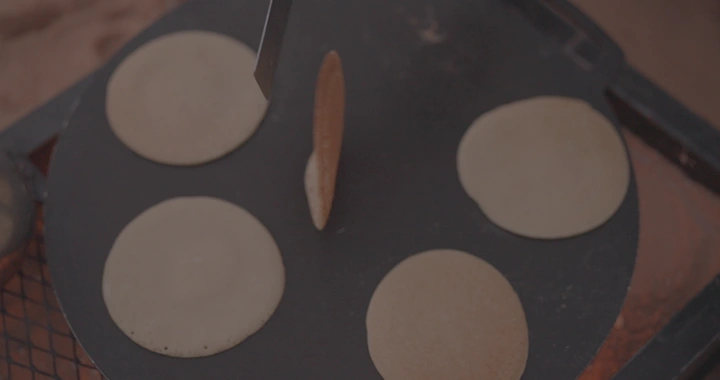 رغفان تُطهى على الصاج في مطبخ خارجي، لقطة قريبة.