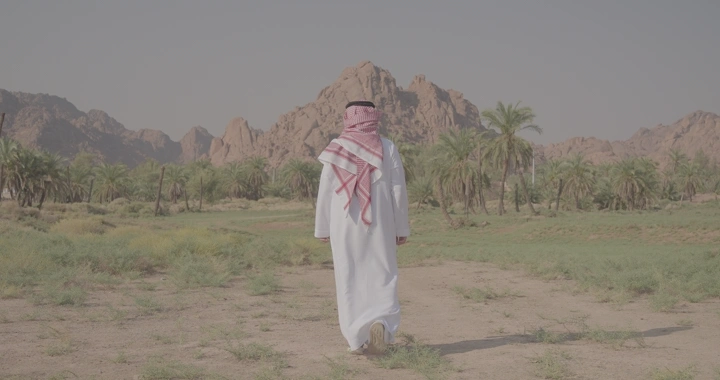 رجل يرتدي الزي التقليدي يمشي نحو جبال عقدة في حائل، لقطة خلفية.
