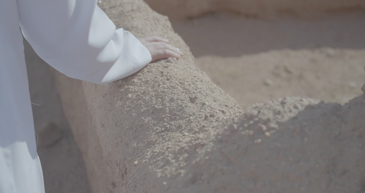 يد تلمس جدار بيت طيني في ضوء الشمس، لقطة قريبة.