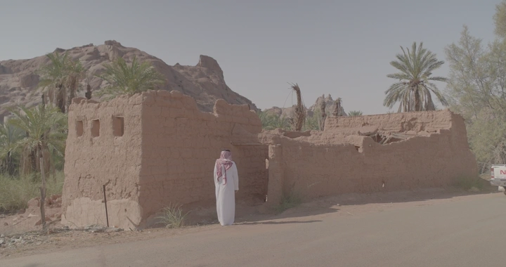 بيت طين قديم في الصحراء مع نخيل، لقطة نهارية.