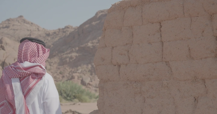 رجل يرتدي الزي التقليدي بجانب جدار طيني في الصحراء، لقطة جانبية.