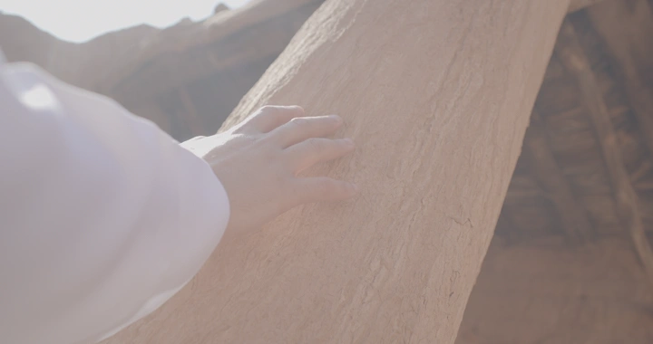 يد تلمس جدار بيت طيني تحت ضوء الشمس، لقطة قريبة.