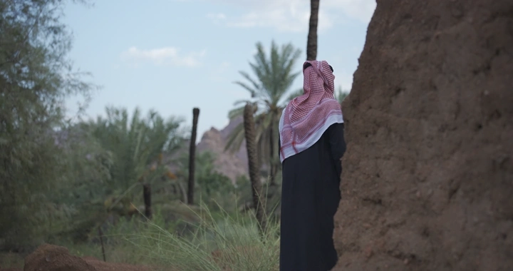 رجل بجانب بيت طين ونخل في منطقة صحراوية، لقطة طبيعية.