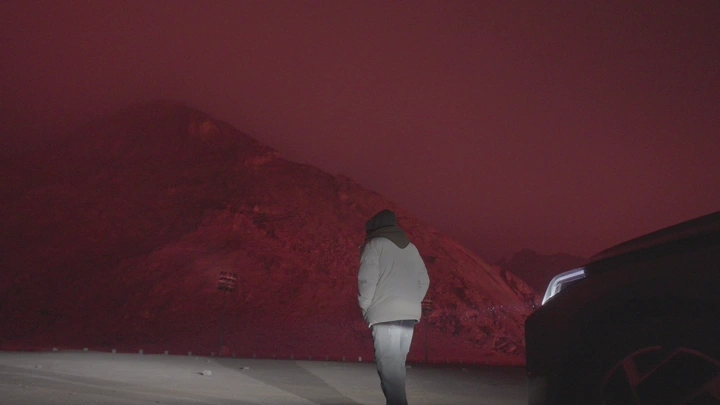 شخص يقف أمام جبل مضاء بضوء أحمر في الليل، لقطة ليلية.