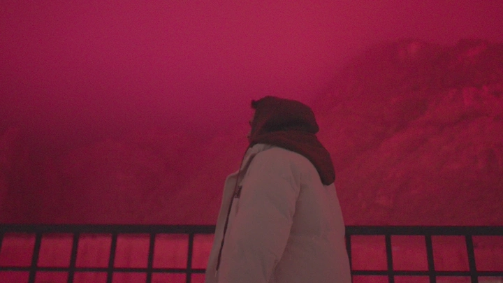 شخص يقف أمام جبال عقدة في ضباب حائل، إضاءة حمراء.