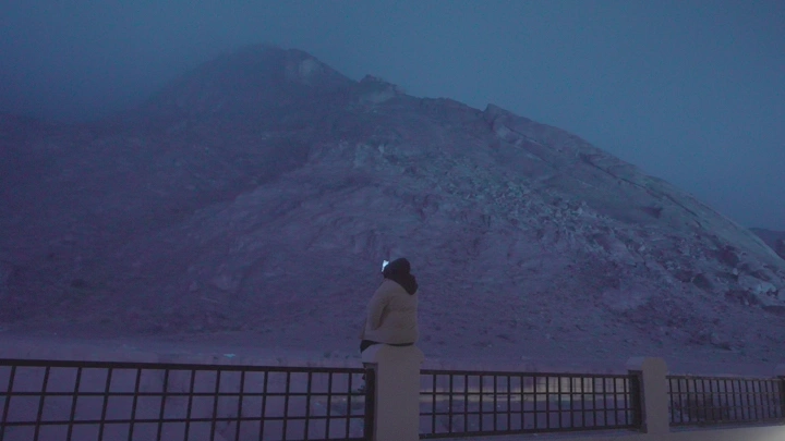 شخص يجلس أمام جبال عقدة في حائل تحت الضباب، تصوير ليلي.