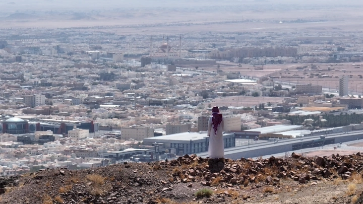 شخص يقف على تلة تطل على مدينة حائل، لقطة من الخلف.