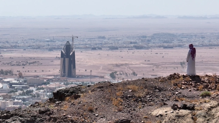 رجل ينظر إلى مدينة حائل من تلة صخرية، لقطة بعيدة.