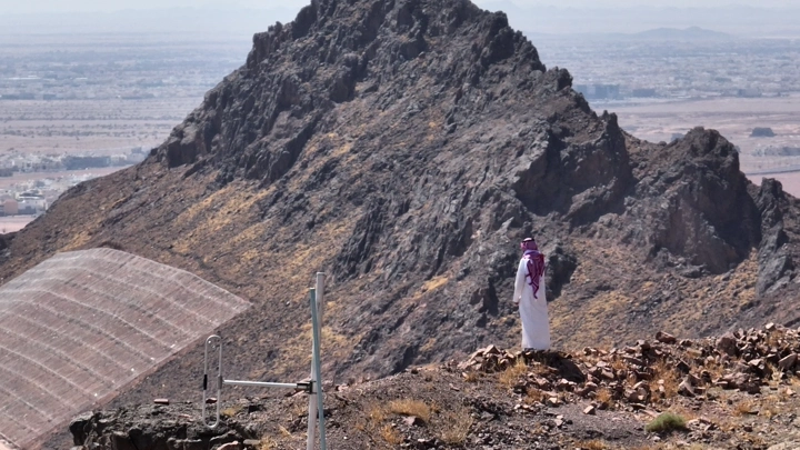 رجل يرتدي الثوب يقف أمام جبل في حائل، لقطة بعيدة.
