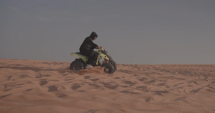 شخص يقود دراجة رباعية في الصحراء، لقطة جانبية.