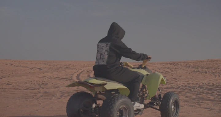 شخص يقود دراجة رباعية في الصحراء، لقطة من الخلف.
