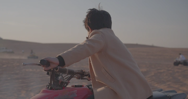 شخص يقود دراجة رباعية في الصحراء، لقطة من الخلف.