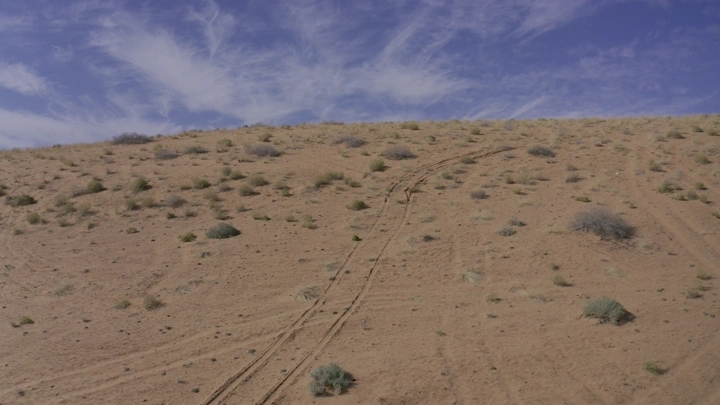 صحراء رملية مع آثار إطارات تحت سماء زرقاء، لقطة نهارية.