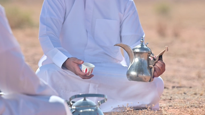 شخص يقدم القهوة السعودية في الصحراء، لقطة قريبة.