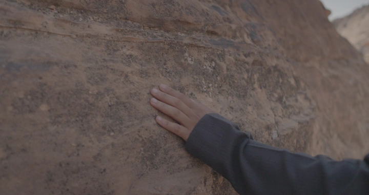 يد تلمس صخرة جبلية في النهار، لقطة قريبة.