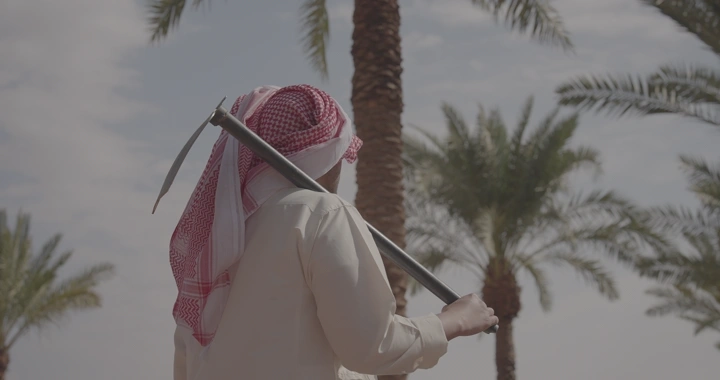 مزارع يحمل محراثًا في بستان نخيل، لقطة نهارية.