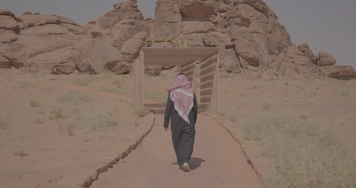 شخص يمشي نحو جبل أم سنمان في جبة حائل، لقطة من الخلف.