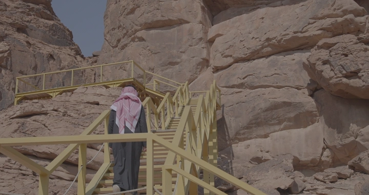 رجل يصعد درجًا خشبيًا في جبل أم سنمان في جبة حائل، لقطة نهارية.