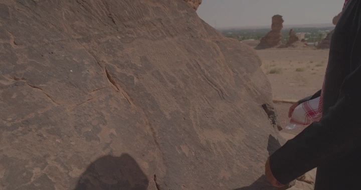 يد تلمس نقوش ثمودية في جبة حائل، لقطة قريبة.