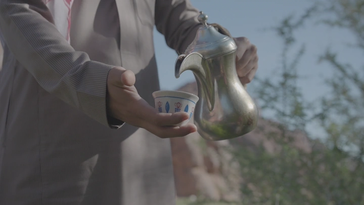 شخص يصب القهوة السعودية في فنجان بالخارج، لقطة قريبة.