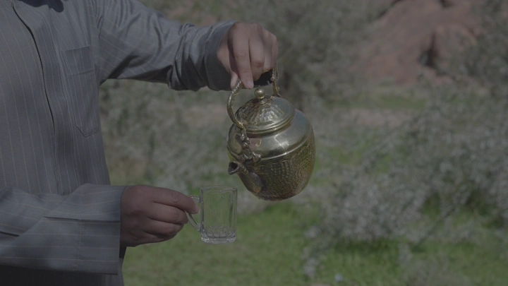 رجل يصب الشاي من إبريق ذهبي في كاسه زجاجية بالخارج، لقطة مقربة.