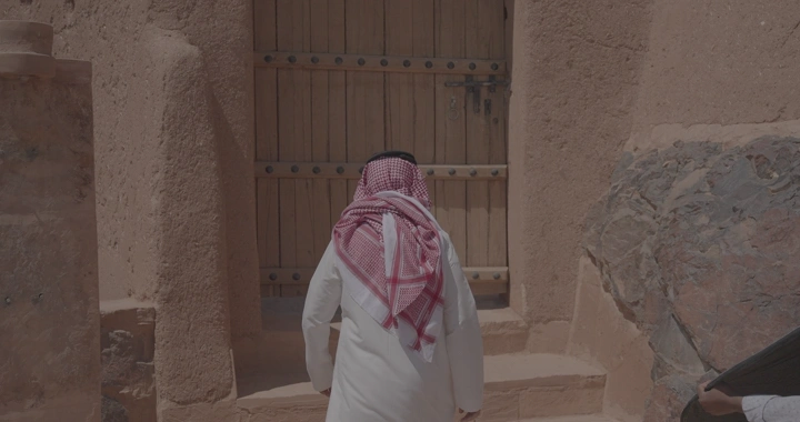 رجل يرتدي الزي السعودي ويفتح باب قلعة عيرف في حائل، لقطة نهارية.