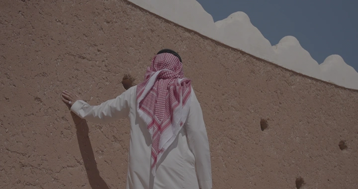 رجل يرتدي الزي التقليدي يلمس جدار قلعة عيرف، لقطة نهارية.