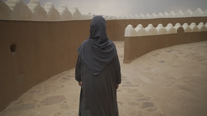 امرأة تسير في قلعة عيرف بحائل، لقطة من الخلف.