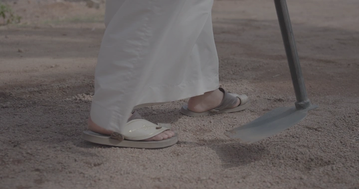 شخص يرتدي ثوب ابيض يستخدم مجرفة في الأرض، لقطة قريبة.