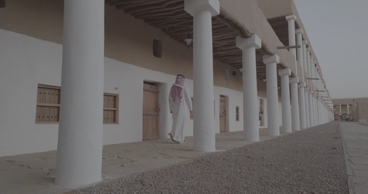 رجل يمشي بجانب أعمدة قصر القشلة في حائل، لقطة من مستوى الأرض.