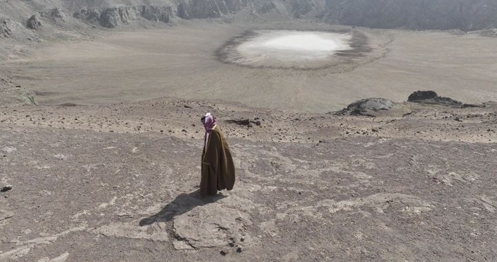شخص يسير أمام فوهة بركان الهتيمه في حائل، لقطة جوية.