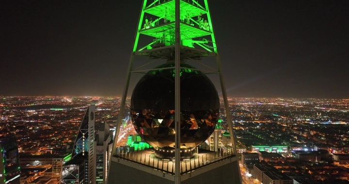 برج الفيصلية مضاء باللون الأخضر في الرياض ليلاً، لقطة جوية.