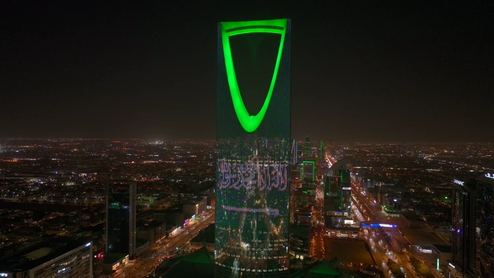 برج المملكة مضاء باللون الأخضر في الرياض ليلاً، لقطة جوية.