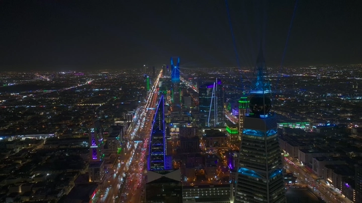 منظر جوي لمدينة الرياض ليلاً مع برج المملكة مضاء بالأضواء الزرقاء.