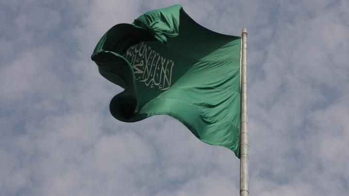 علم أخضر يرفرف في السماء مع غيوم خلفه، لقطة من الأسفل.